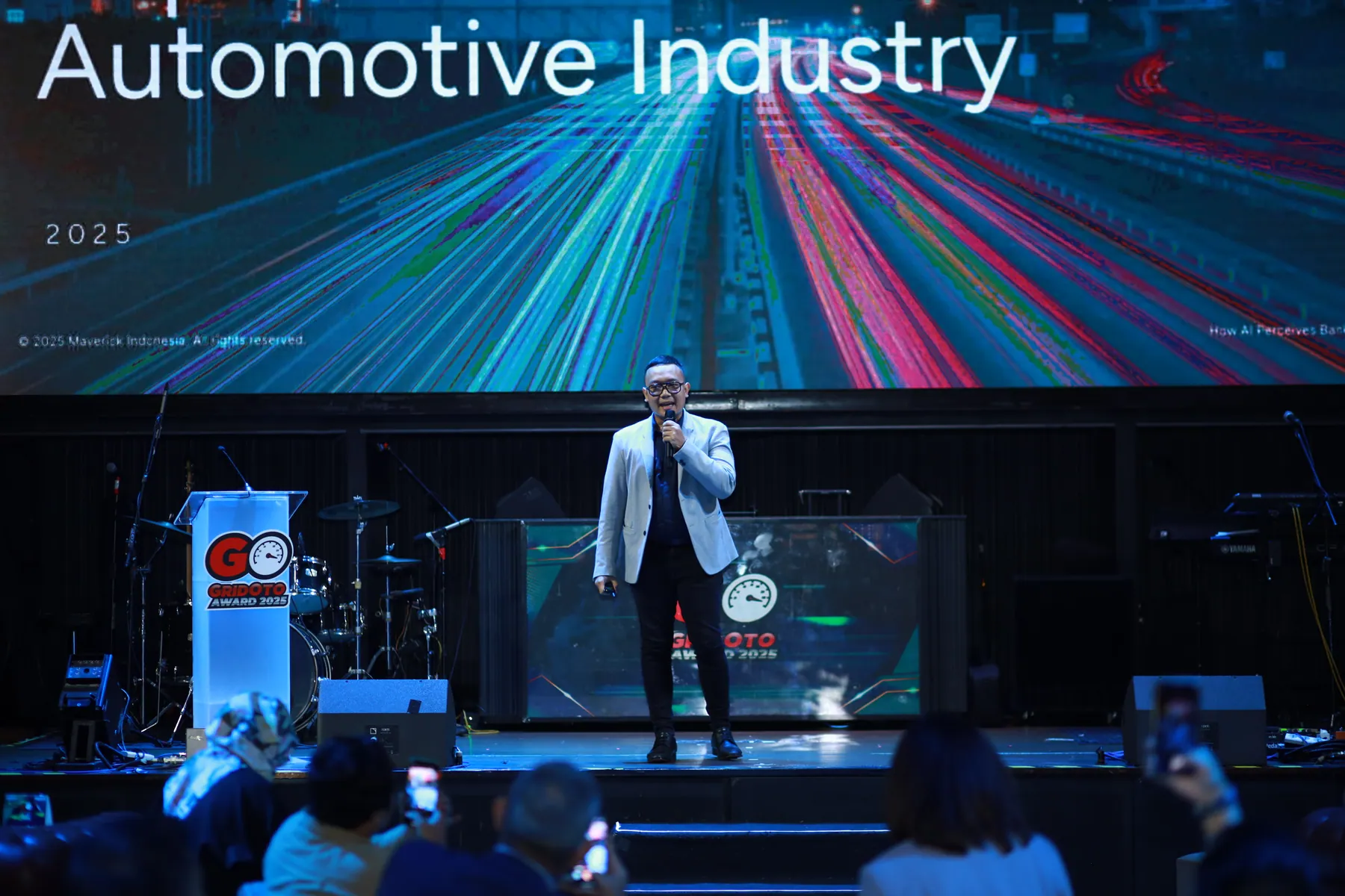 Cahyanto speaking on an automotive industry conference stage in front of a presentation screen.