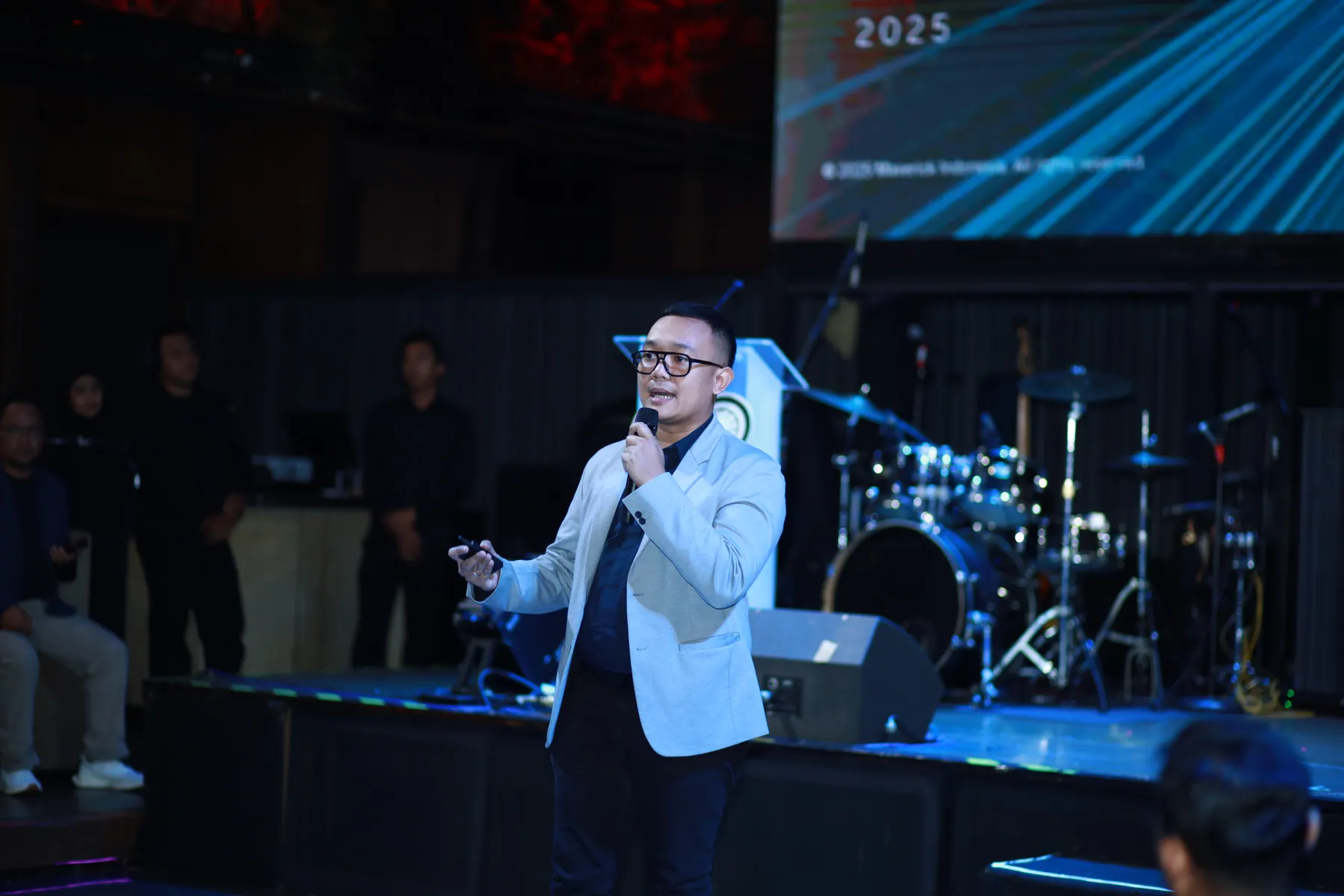 Cahyanto presenting with a microphone and clicker on stage.